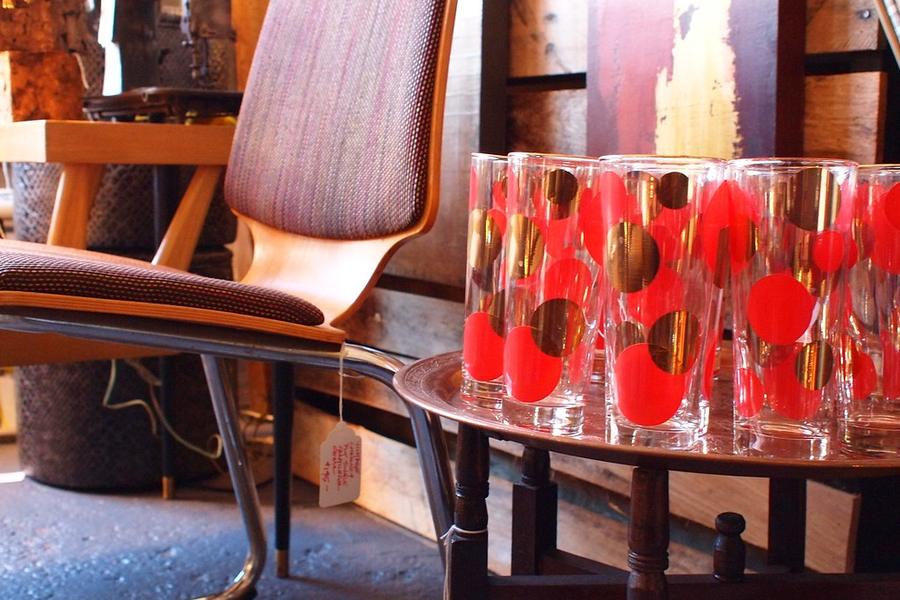 A tray of red-and-gold vintage glassware beside a mid-century chair