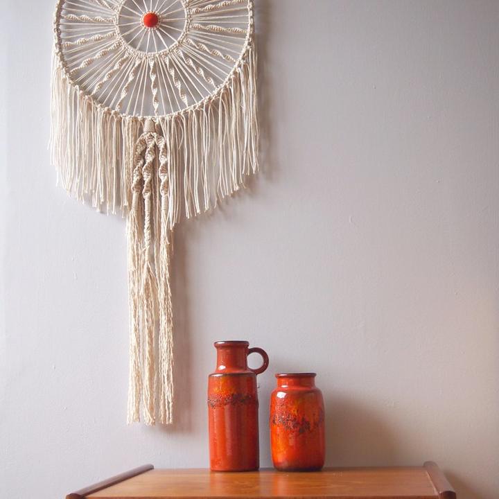 A macramé hanging above a teak table with orange ceramics